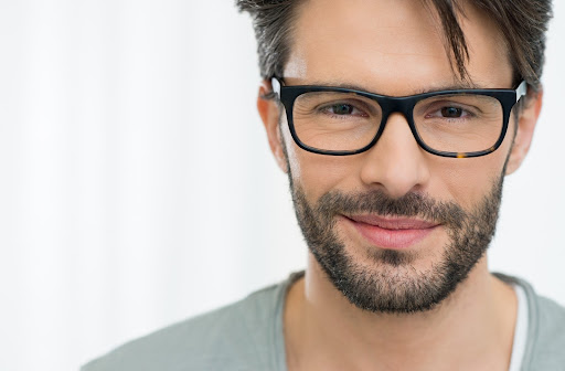 Handome man with dark eyes and short beard wearing perfectly fitting dark rimmed glasses staring straight into the camera