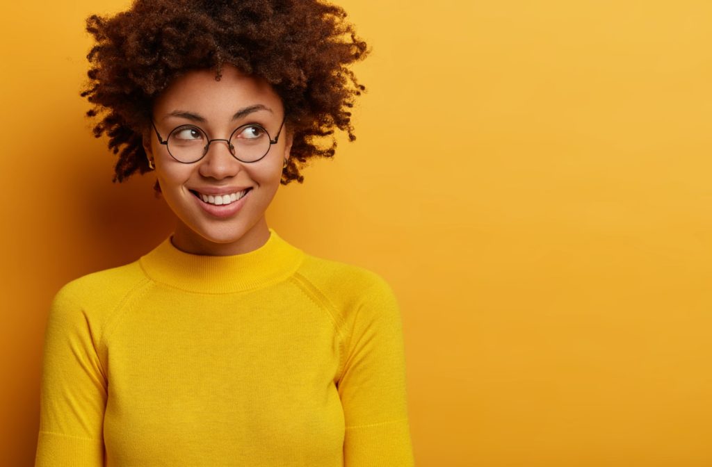 A young woman wearing glasses and smiling, against a yellow backdrop