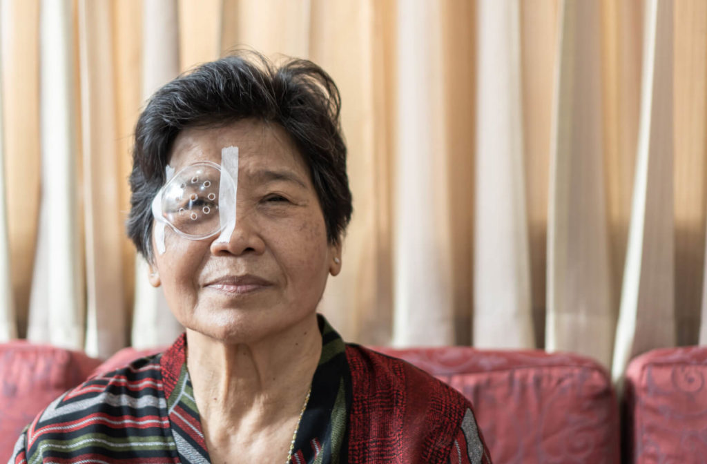 An old woman sitting on a couch with a clear plastic ventilated shield protecting her right eye.