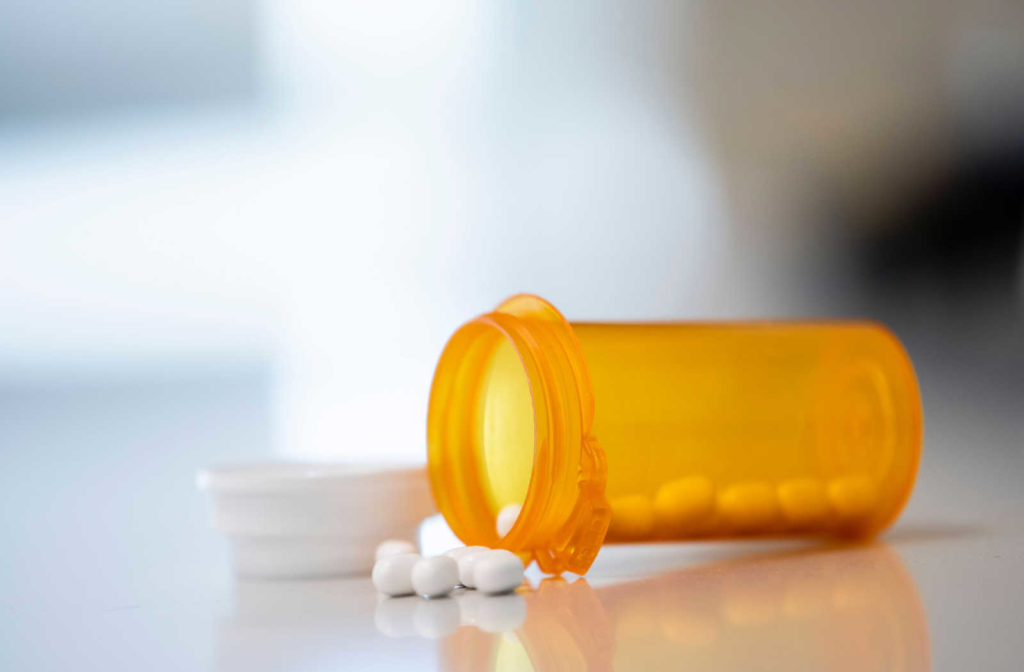 An orange prescription pill bottle laying on a counter with white pills spilled out of it