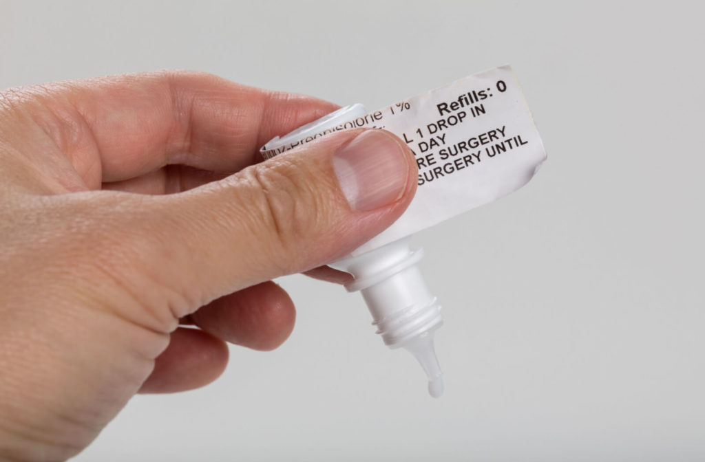 A close-up of a man's hand holding a  bottle of eye drops with written instructions.