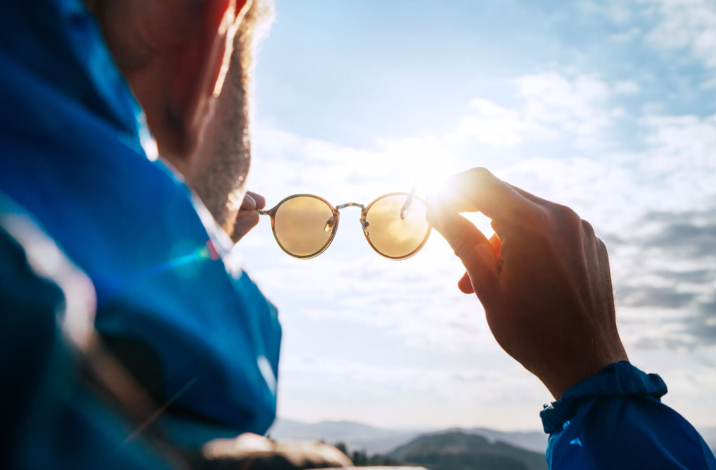 A man outdoors holding a polarized sunglasses directly into the sun.