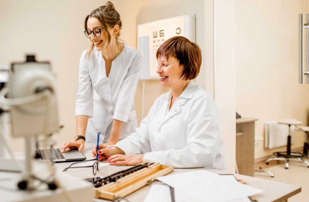 An optometrist and optician looking at a laptop, smiling while working together