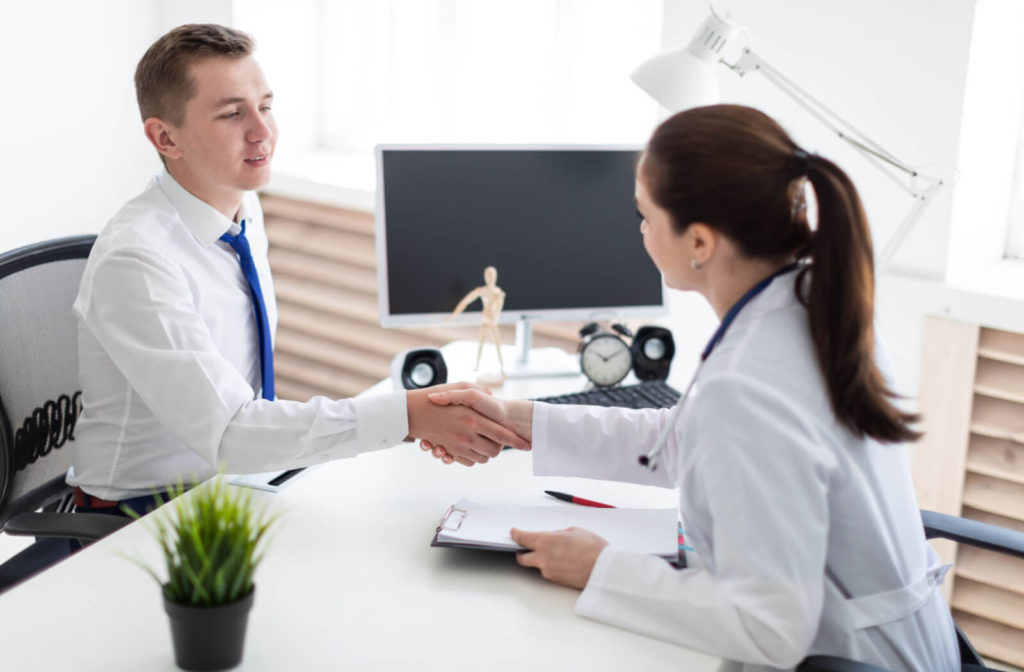 A female optometrist shaking the hands of a young man in an office