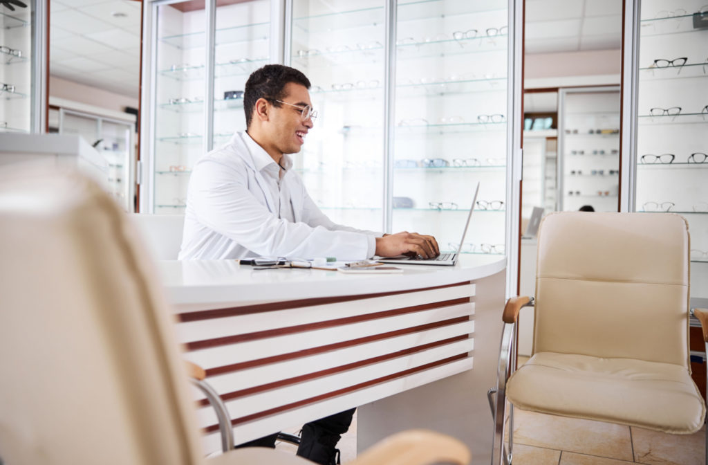 An optometrist in his clinic sitting and working on a computer.