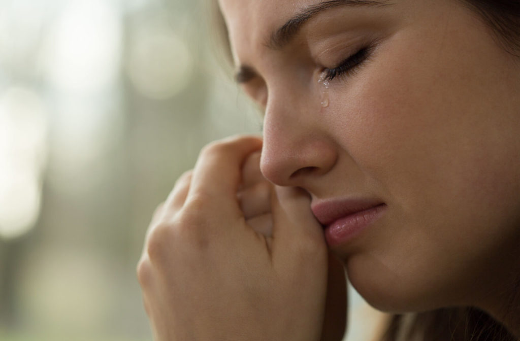 A close-up of a woman crying with closed eyes.