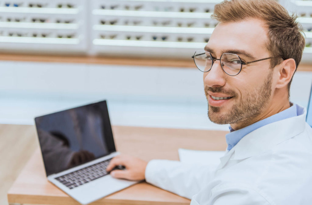 A male optometrist working on a laptop while smiling.