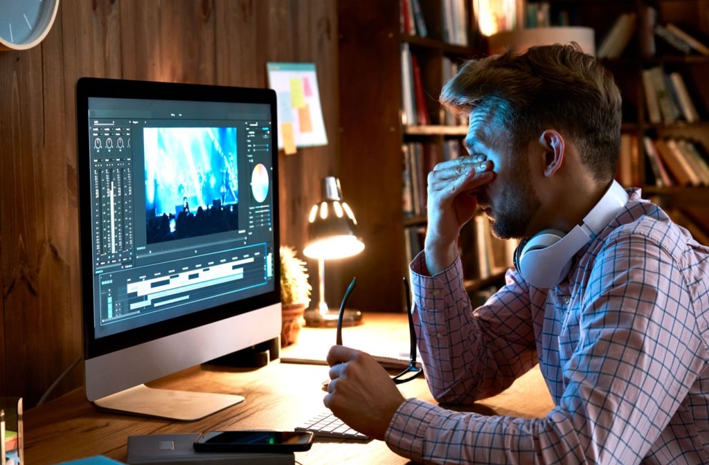 A young businessman, tired and overworked, removes his glasses and rubs his tired, dry eyes after spending long hours working on his computer late into the night.