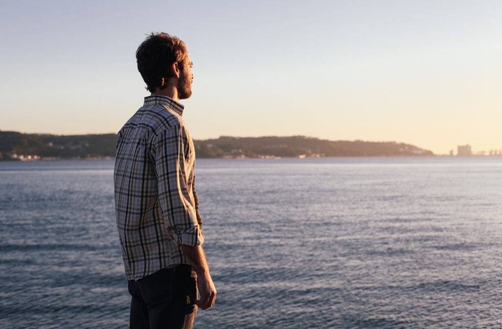 A young man watching the sun set over a lake looking far into the distance.