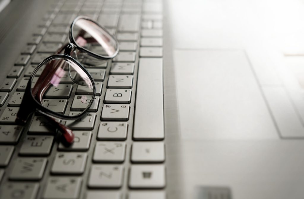 Close-up of a laptop keyboard with a pair of glasses resting on the keys.