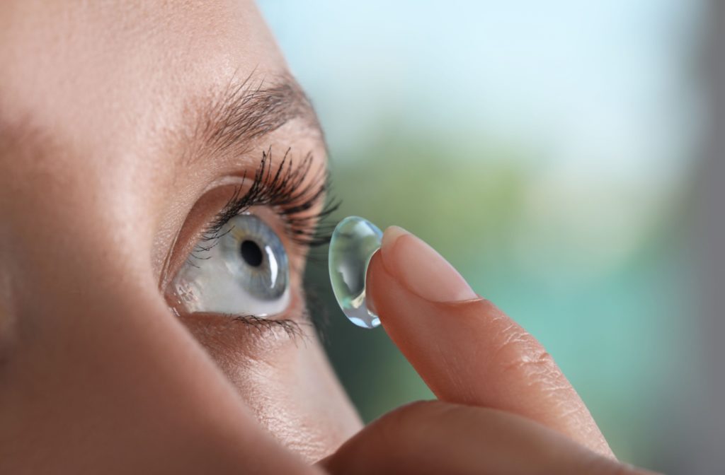 A close-up of a patient putting a contact lens on their left eye using their index finger.