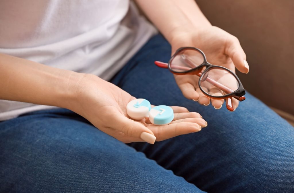 Person holding a pair of eyeglasses in one hand and a contact lens case in the other, representing the choice between glasses and contact lenses.