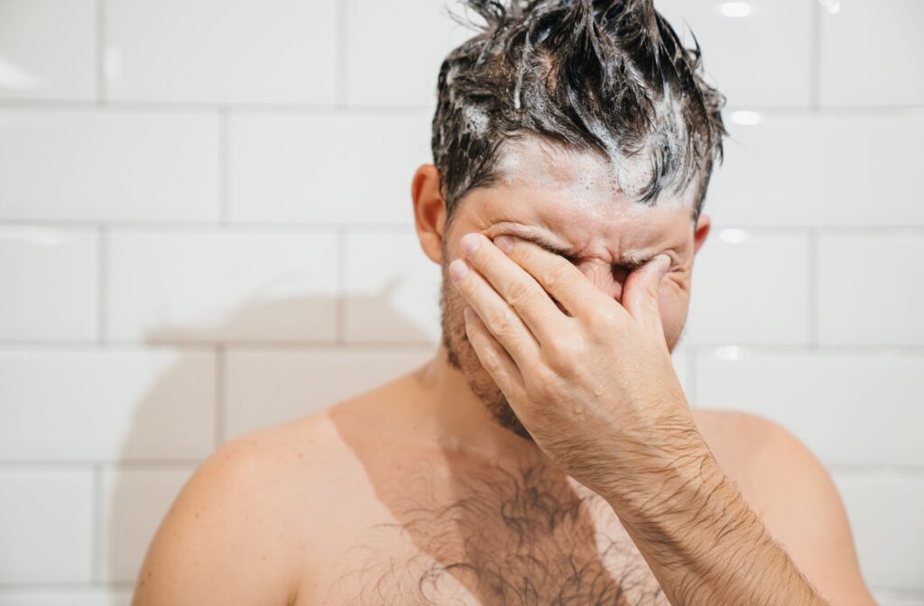 Man in shower gets soap in his eyes causing discomfort.