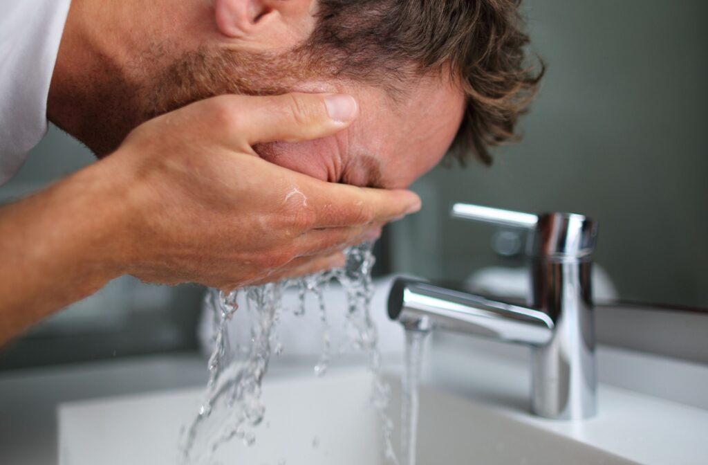 Man rinsing his eyes with clean water over a sink, demonstrating first aid steps after getting soap in the eyes.