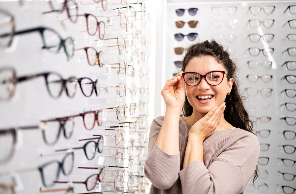 A smiling adult tries on frames in their eye doctor's showroom.
