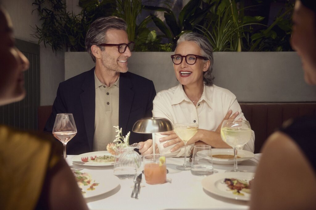 A couple in a loud restaurant wearing Nuance Audio glasses to help see and hear better in their environment.
