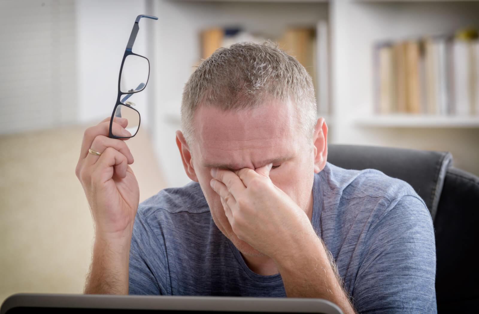 A person rubbing their eyes due to vision issues from high blood pressure.